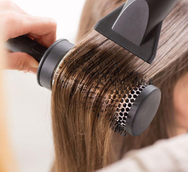 hairdresser using large round brush and hair dryer to dry long hair