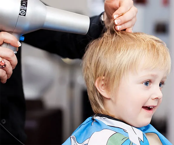 children’s hair cuts young boy with blond hair and blue eyes having his hair blow dried