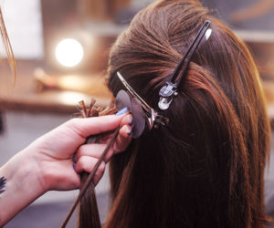 hairdresser putting in hair extensions in lady's long brown hair