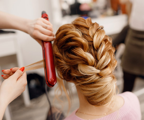 lady with blond hair with intriciate up-do and hairdresser using straightening iron