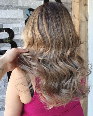 woman in purple t-shirt with light brown hair after caramel balayage