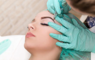microblading expert with green glove doing eyebrow microblading on a woman's eyebrows