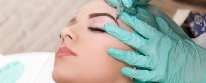 microblading expert with green glove doing eyebrow microblading on a woman's eyebrows