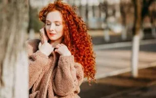 Woman with long red curly hair standing next to a tree